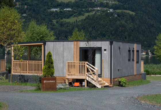 Lodge Enzian junto al lago con fachada moderna de madera, terraza, árboles y montañas de fondo.