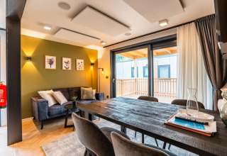Salón moderno en la lodge Enzian en Ossiacher See, Austria, con mesa de comedor, sofá y acceso al balcón.