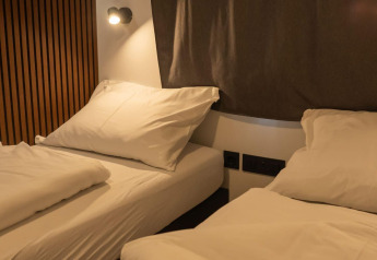 Dos camas individuales con sábanas blancas y almohadas en Enzian Lodge, Ossiacher See, Austria, de noche.