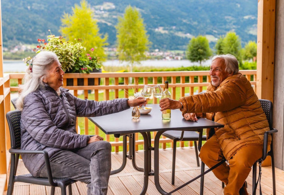 Pareja mayor brinda con vino en la terraza de Enzian Waterfront con vista al lago Ossiacher See en Austria.