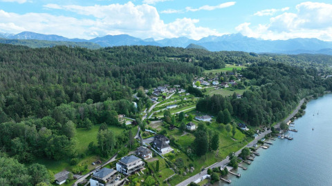 Vista aerea di un alloggio glamping tra lago, colline verdi e montagne sullo sfondo, immerso nella natura.