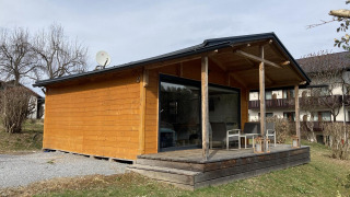 Buitenaanzicht van Stuga 2, een houten chalet met terras, stoelen en lantaarns in een rustige omgeving.