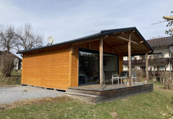 Vista exterior de Stuga 2, una acogedora cabaña de madera con terraza y sillas en un entorno tranquilo.
