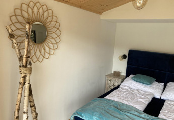 Schlafzimmer in Stuga 2 am Wörthersee, Österreich, mit Doppelbett, Holzdecke und dekorativem Spiegel.