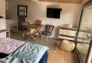 Interior of cozy lodge Stuga 2 at Wörthersee, Austria, featuring dining area, TV, armchairs, and pouf.