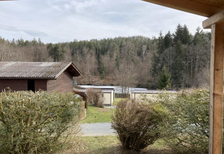 View from Stuga 2 at Wörthersee, Austria, showing wooden lodges, shrubs, and a forested hillside nearby.