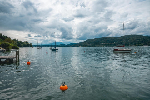 Vista del Wörthersee con barche a vela e montagne, scattata dal lodge Stuga 2 in Austria, in una giornata nuvolosa.