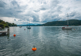 Blick auf den Wörthersee mit Segelbooten und Bergen von der Lodge Stuga 2 in Österreich an einem bewölkten Tag.