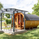 Traktorhytte tiny house med træfacade og rund form, terrasse og to stole i grønne omgivelser.