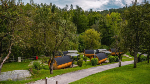 Pequeñas casas tipo cabaña Tractor en Wörthersee, Austria, rodeadas de árboles y césped bajo un cielo nublado.