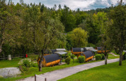 Pequeñas casas tipo cabaña Tractor en Wörthersee, Austria, rodeadas de árboles y césped bajo un cielo nublado.