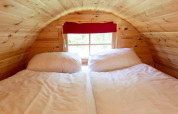 Acogedora cama bajo techo de madera inclinada en Tractor Cabin, Wörthersee, Austria, con ventana y cortina roja.
