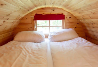 Acogedora cama bajo techo de madera inclinada en Tractor Cabin, Wörthersee, Austria, con ventana y cortina roja.