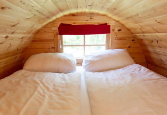 Hyggelig seng under skrå loft i Tractor Cabin på Wörthersee, Østrig, med træpaneler og vindue.