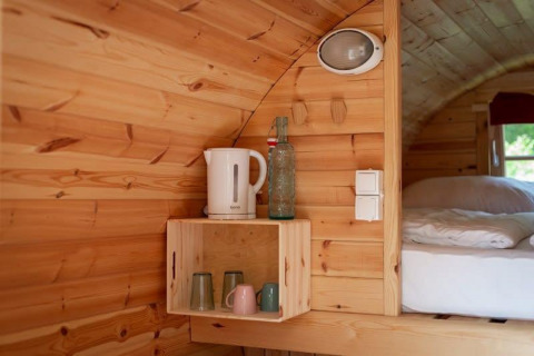 Acogedor interior de madera en una tiny house con hervidor, vasos y cama en Tractor cabin, Wörthersee, Austria.