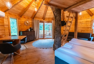 Acogedora casa del árbol en Wörthersee, Austria, con interior de madera, escalera y vistas al bosque.