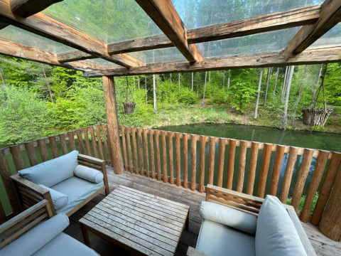 Acogedora terraza de madera con sofás y vista a lago y bosque en Treehouse at Wörthersee, Austria.