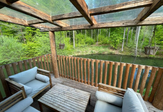 Acogedora terraza de madera con sofás y vista a lago y bosque en Treehouse at Wörthersee, Austria.