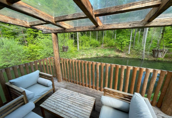 Hyggelig terrasse med træmøbler og udsigt over sø og grøn skov ved Treehouse at Wörthersee, Østrig.