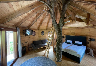 Vista interior de la Treehouse en Wörthersee, Austria, con tronco de árbol, suelo de madera y decoración moderna.