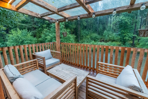 Terraza de madera con cómodos asientos y vistas al bosque junto al Treehouse at Wörthersee en Austria.