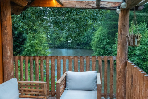 Terraza de madera con sillones y vista a un lago y bosque en Treehouse en Wörthersee, Austria.