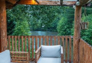 Terraza de madera con sillones y vista a un lago y bosque en Treehouse en Wörthersee, Austria.