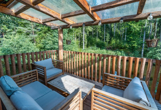 Terraza de casa del árbol en Wörthersee, Austria, con asientos cómodos y vista al bosque verde.