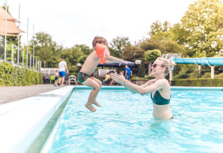 Madre juega con su hijo en una piscina de un alojamiento glamping, rodeados de árboles y tobogán.