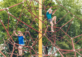 Dos niños juegan y trepan por una gran estructura de cuerdas en el parque de una estancia glamping.
