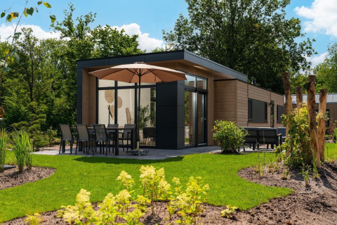 Lodge moderno Cannenburch en Veluwepark de Bosgraaf, Países Bajos, con terraza, sombrilla y jardín verde.