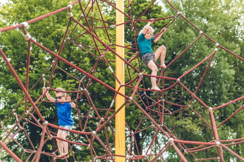 Dos niños escalan una gran estructura de cuerdas en un parque infantil de un alojamiento glamping.