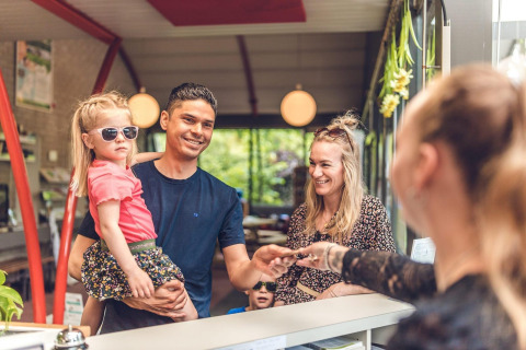 Una familia sonriente hace el check-in en la recepción de un alojamiento glamping, atendida por personal.