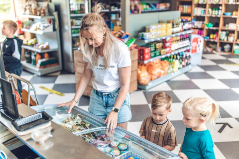 Una mujer y dos niños eligen helado de un congelador en una tienda durante su estancia de glamping.