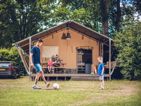 Familia disfrutando delante de una tienda safari en Veluwepark de Bosgraaf, Países Bajos, jugando al fútbol.