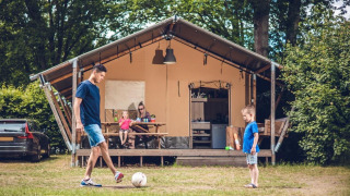 Familie foran en safaritelte ved Veluwepark de Bosgraaf i Holland, spiller fodbold og nyder tiden sammen.