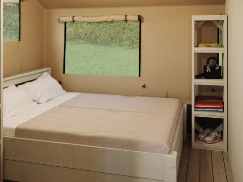 Dormitorio en tienda Safari Ranger Lodge con cama doble, estanterías y ventana en Veluwepark de Bosgraaf, Países Bajos.