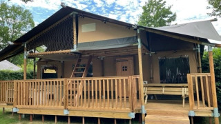 Tenda safari chiamata Ranger Lodge con veranda in legno, rete, panchina e circondata da alberi verdi.