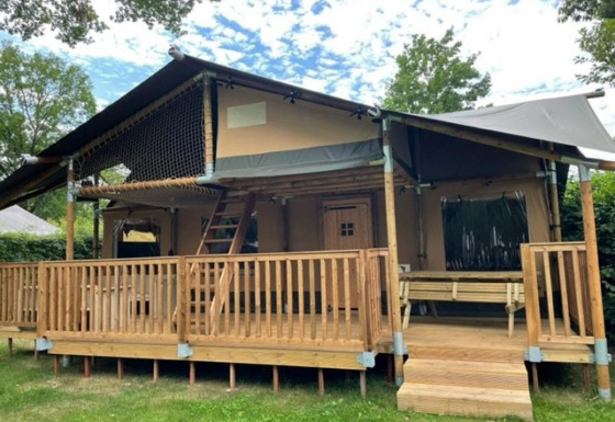 Tienda safari llamada Ranger Lodge con terraza de madera, banco y rodeada de césped y árboles verdes.