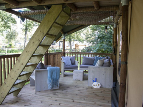 Terraza cubierta de madera con muebles rústicos y escalera en una tienda safari en Veluwepark de Bosgraaf, Países Bajos.