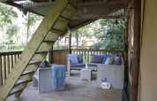Überdachte Holzterrasse mit gemütlichen Sitzmöbeln und Holztreppe in einem Safarizelt im Veluwepark de Bosgraaf.