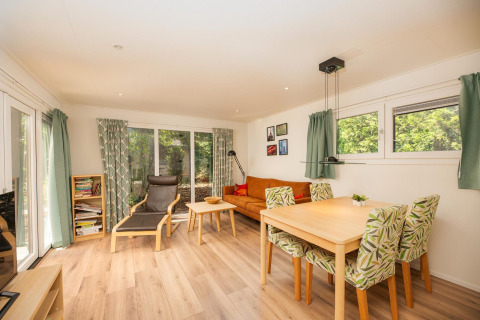 Helles Wohnzimmer der Veluwe Lodge im Veluwepark de Bosgraaf, Niederlande, mit Essbereich, Sofa und großen Fenstern.