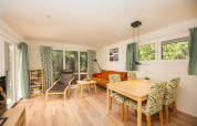 Helles Wohnzimmer der Veluwe Lodge im Veluwepark de Bosgraaf, Niederlande, mit Essbereich, Sofa und großen Fenstern.