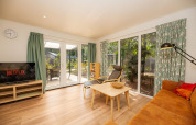 Modernes Wohnzimmer in der Veluwe Lodge im Veluwepark de Bosgraaf, Niederlande, mit großen Fenstern.