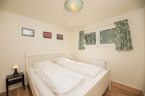 Dormitorio con cama doble, paredes blancas, cortinas verdes y mesa de noche en Veluwe Lodge, Países Bajos.