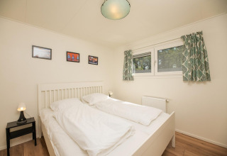 Dormitorio con cama doble, paredes blancas, cortinas verdes y mesa de noche en Veluwe Lodge, Países Bajos.
