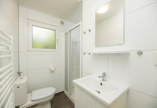 Baño moderno blanco con ducha, lavabo, inodoro, ventana y espejo en Veluwe Lodge, Países Bajos.