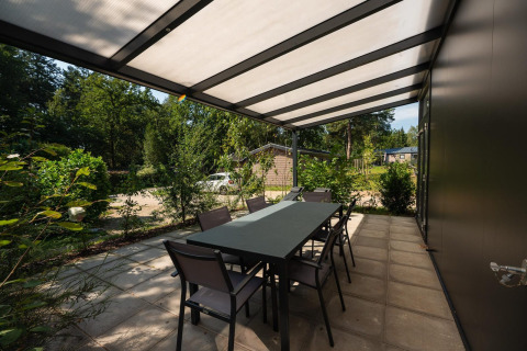 Terraza cubierta con mesa de comedor en Forest Lodge de Veluwepark de Bosgraaf en los Países Bajos, rodeada de naturaleza.