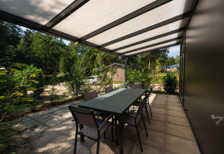 Terraza cubierta con mesa de comedor en Forest Lodge de Veluwepark de Bosgraaf en los Países Bajos, rodeada de naturaleza.