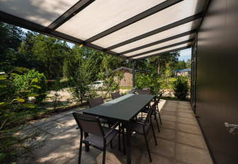 Overdækket terrasse med spisebord ved Forest Lodge på Veluwepark de Bosgraaf i Holland, omgivet af natur.